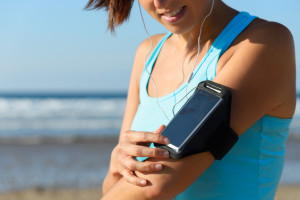 Sporty woman touching phone screen in arm sport band before running on beach. Female athlete listening music while doing sport.